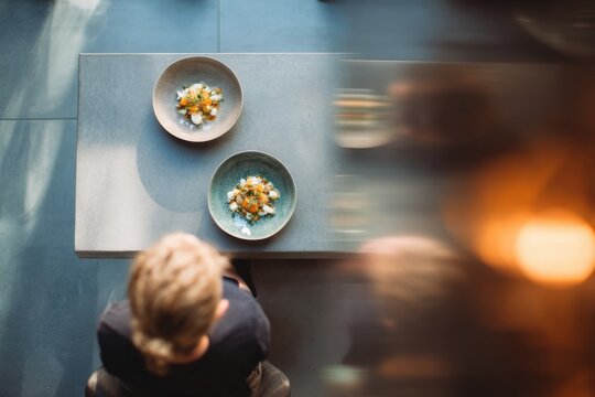 Woman sitting at table with gourmet food plates. Overhead view of fine dining experience in modern restaurant. Culinary art and gastronomy concept for luxury lifestyle advertisement.