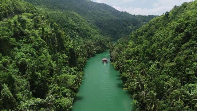 Aerial view of the Loboc River Cruise boat navigating through the lush tropical jungle and emerald green waters of the river in Loboc, Central Visayas, Philippines.