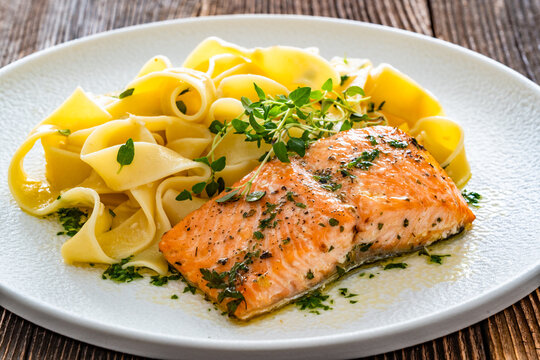 Pasta with baked salmon steak on wooden table
