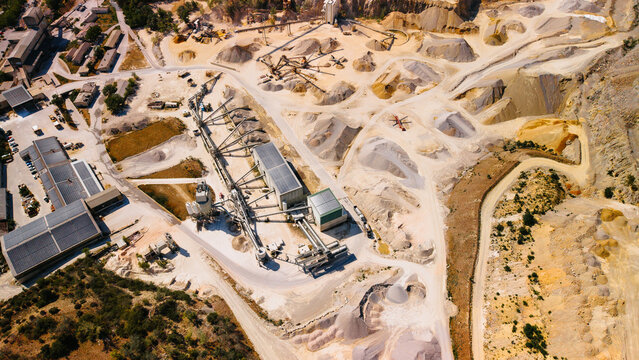 Aggregate processing plant inside sand quarry from above. High angle drone frame shows conveyors, roof mounted solar panels, storage piles, trucks and access roads.