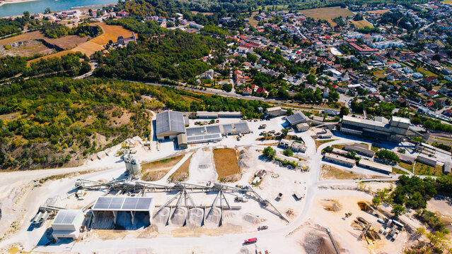 Aerial view of sand quarry processing plant with solar panels. Industrial facility with sand piles, machinery and nearby village under bright daylight.