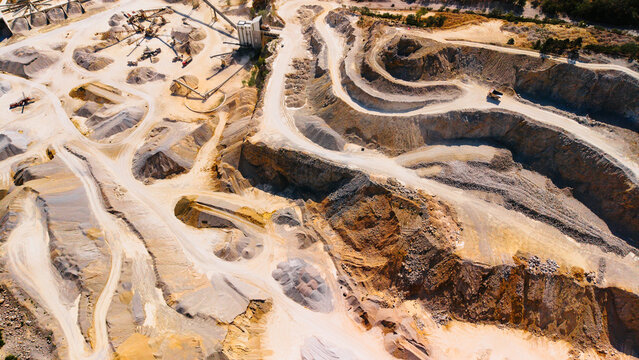 Sand quarry mining site with conveyor belts and terraced slopes. Mining operation featuring stone terraced walls, conveyor systems, sand heaps and trucks.