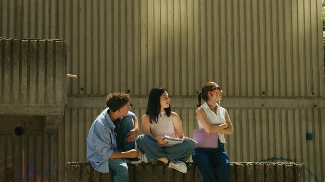 Three high school students are studying and conversing outdoors. They are collaborating and sharing ideas together outside.