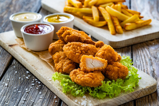 Breaded chicken nuggets with French fries and mayonnaise, ketchup, mustard on wooden table
