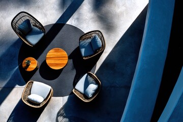 Fototapeta premium Wicker armchairs arranged around wooden table on terrace. Top view of outdoor furniture set on round rug. Modern patio decor with minimalist design and dramatic shadows. Architectural space.