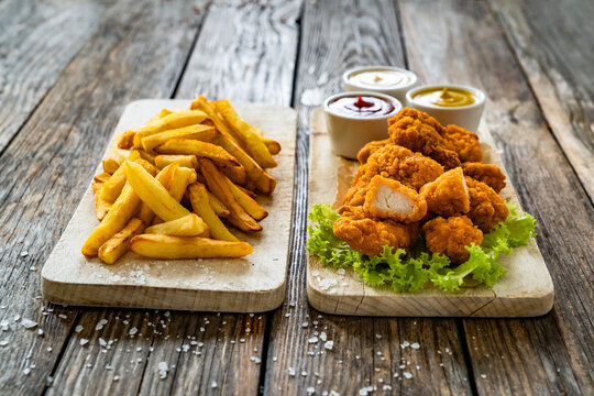 Breaded chicken nuggets with French fries and mayonnaise, ketchup, mustard on wooden table
