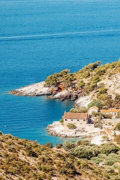 View of a stone building nestled in a coastal cove with pine trees and clear blue water in Hvar, Split-Dalmatia County, Croatia.