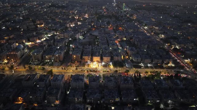 Aerial night view of an urban landscape in Syria featuring glowing city lights and illuminated streets.  Post-war Syrian cityscape and daily life at night.