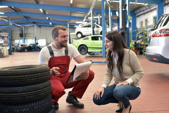 mechanic and customer talking to each other in a garage - changing tyres from the car