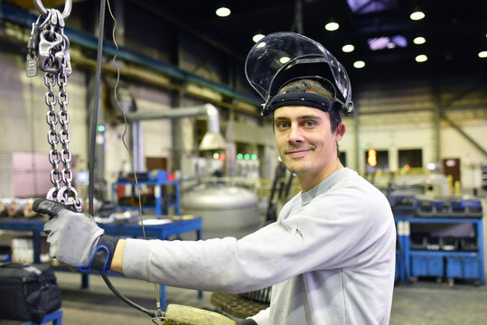 portrait of young smiling industrial worker with helmet in a modern industrial hall at his workplace