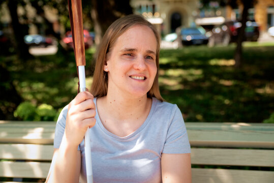 Blond haired blind woman with white cane sitting in a public park