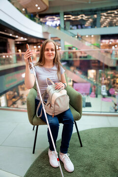 Confident blind woman with white cane sitting on a bench in a shopping mall