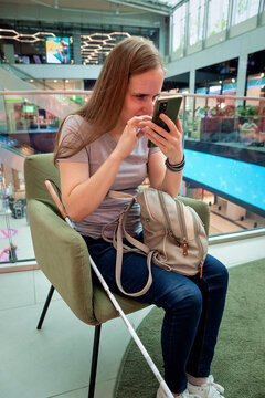 Visually impaired woman with white cane using smartphone app in shopping mall