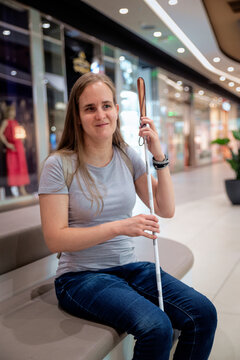Confident blind woman with white cane sitting on a bench in a shopping mall