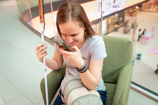 Visually impaired woman with white cane using smartphone app in shopping mall