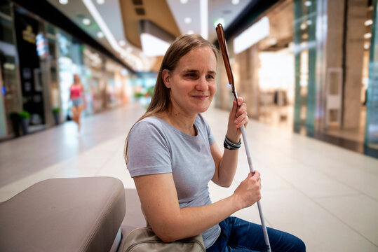 Confident blind woman with white cane sitting on a bench in a shopping mall
