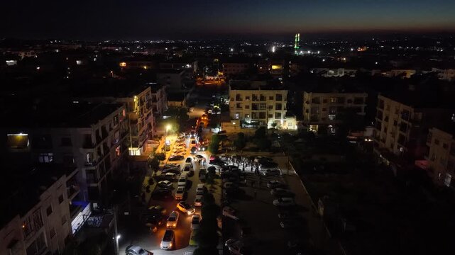 Aerial night view of an urban landscape in Syria featuring glowing city lights and illuminated streets.  Post-war Syrian cityscape and daily life at night.