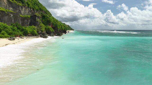 Beautiful aerial view of Pandawa Beach with white sand, turquoise ocean waves, and green limestone cliffs in Bali, Indonesia.