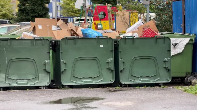 Green dumpsters overflowing with cardboard boxes and paper waste outdoors, full trash containers, recycling, waste management, pollution.