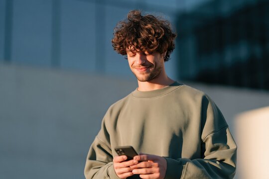 Young man smiling at smartphone outdoors in warm sunlight for lifestyle social media banner and profile background