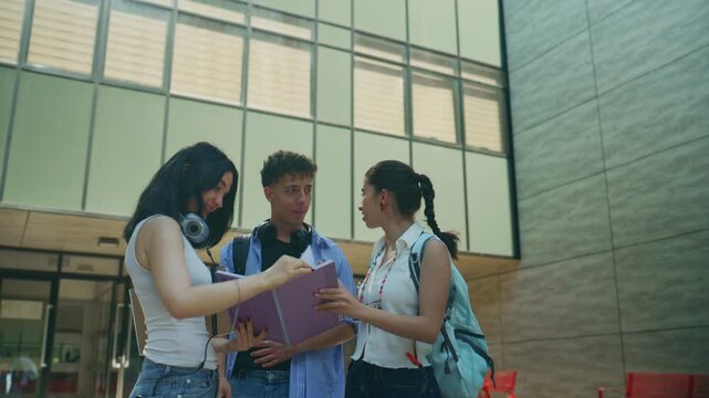 High school students study together, reviewing notes outside a modern building. They are collaborating and discussing lessons.