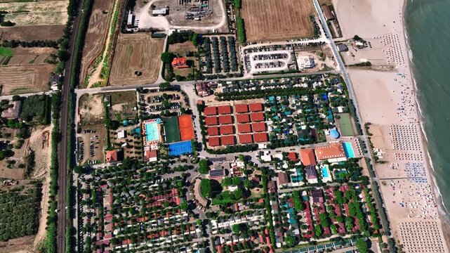 Aerial view of a large holiday resort featuring swimming pools, tennis courts, and rows of cabins situated along the sandy beach in Porto San Giorgio, Marche, Italy.