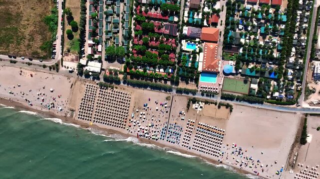Aerial view of the beach resort in Porto San Giorgio with rows of umbrellas, swimming pools, and people relaxing on the sand in Porto San Giorgio, Marche, Italy.