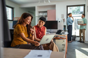 Fototapeta premium Diverse women collaborating on laptop in modern startup office