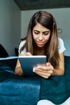 A young woman using a tablet on a bed in a cozy indoor setting
