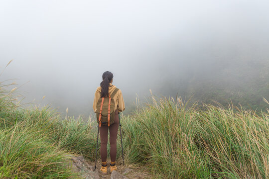 Hiker standing in grassy field surrounded by mountain fog