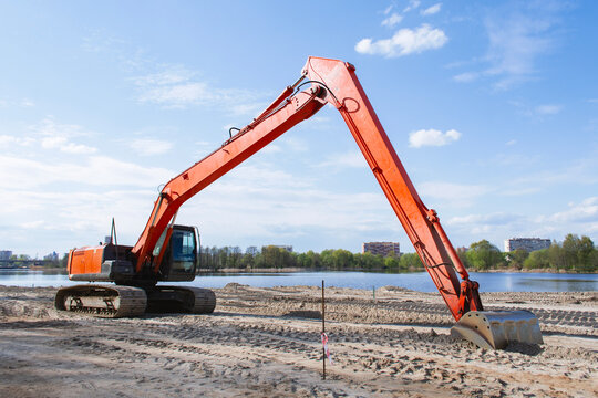 Long reach excavator working on a sandy construction site beside a lake, representing earthmoving, excavation, heavy machinery, infrastructure development and civil engineering.