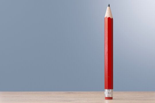 Red wooden pencil standing upright on a light wooden surface against a soft blue background with generous copy space, symbolizing education, creativity, planning, writing and business ideas.