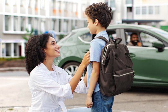 Caring mother adjusting sons backpack before school while father waiting in car