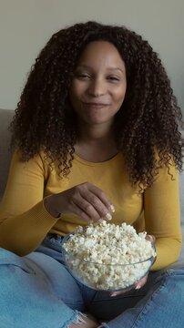 Beautiful african american woman watching tv and eating popcorn