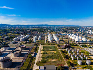 Fototapeta premium Industrial area with storage tanks and pipelines near a city landscape during daylight