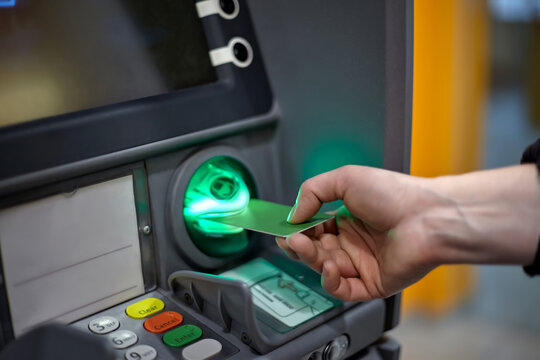 ATM machine credit card insertion process for banking transaction close up shot with illuminated green card reader slot. Hand inserting credit card into ATM reader. Fraud protection, cyber security