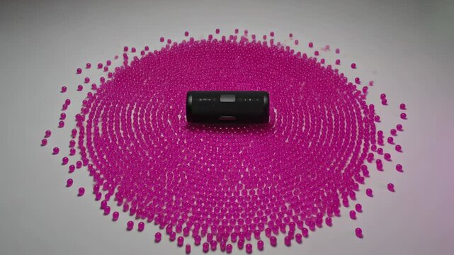 Vibrating black Bluetooth speaker playing music on gray tabletop, rippling pink mat pegs outward
