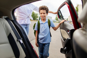 Black schoolboy entering family car after school with his mother nearby © Home-stock