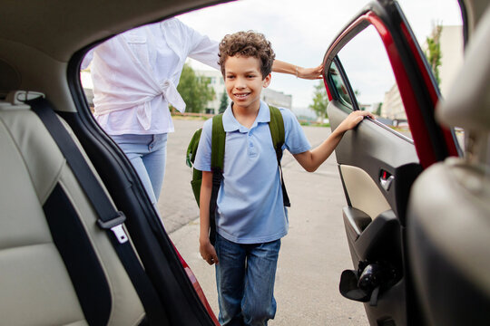 Black schoolboy entering family car after school with his mother nearby