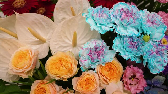Close-up horizontal shot of a vibrant colorful flower arrangement featuring white anthuriums, orange roses, and blue carnations