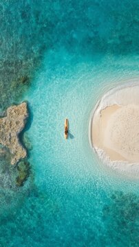 Drone shot of a kayak floating near a sandy beach and rocky area in pristine turquoise waters