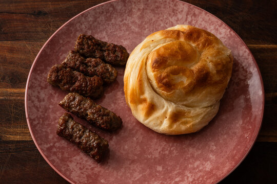 typical Balkan dish consisting of cevapi, grilled minced meat rolls, accompanied by a typical bakery product, burek