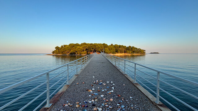 A pier extending toward a small island, surrounded by calm, clear waters. A concept of serenity.