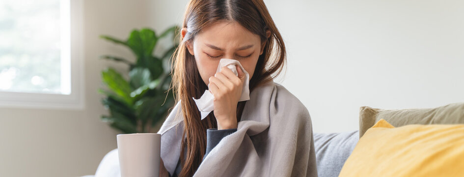 Sick at home concept. Woman sneezing on the sofa in winter season.