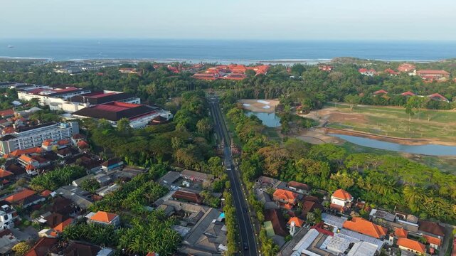 Aerial view of a road surrounded by lush tropical trees and traditional buildings in Kecamatan Kuta Selatan, Bali, Indonesia.