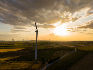 Obraz premium Wind turbines stand tall in the fields during sunset with clouds in the sky and light shining through