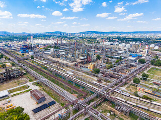 Fototapeta premium Large industrial area with factories, tanks, and train tracks in a city setting under a blue sky
