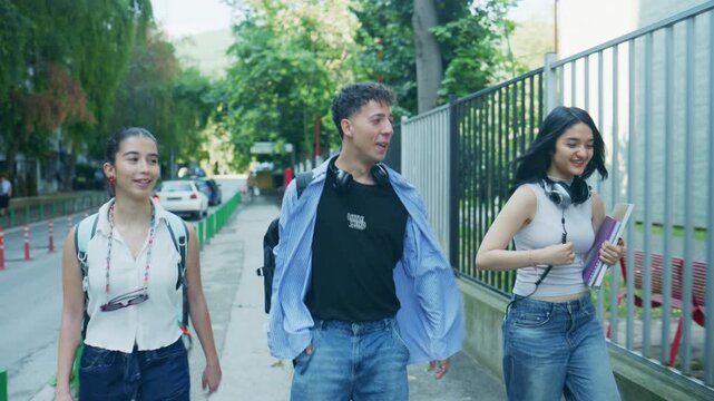 Three happy high school students walk and converse outdoors, carrying backpacks and books. Young friends enjoy a casual stroll and chat together after school.