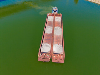 Cargo barge is floating on green water while workers prepare for unloading near the shore in a coastal area during daytime