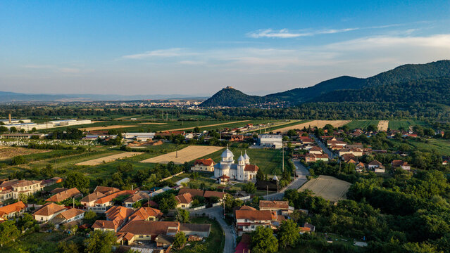 Aerial view of Deva Fortress perched on a hill overlooking the town with a church, houses, and agricultural fields in the rural landscape of Deva, Hunedoara, Romania.